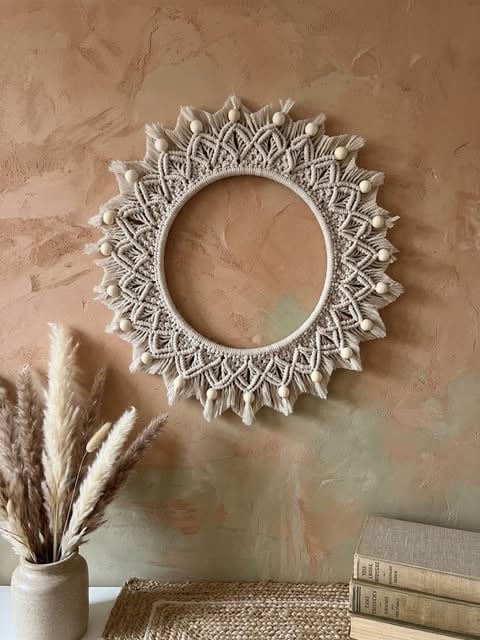 Ornate white circular mirror with detailed carved mandala pattern on textured beige wall above books and dried pampas grass
