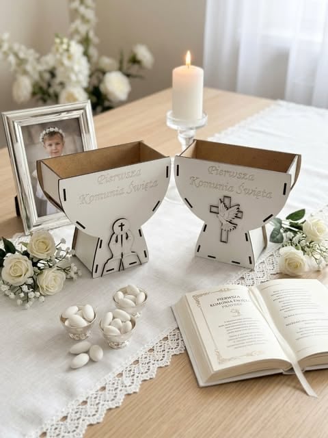Elegant religious commemoration display with two decorative cardboard containers, a lit candle, framed photo, white flowers, prayer book, and candies on a white lace tablecloth